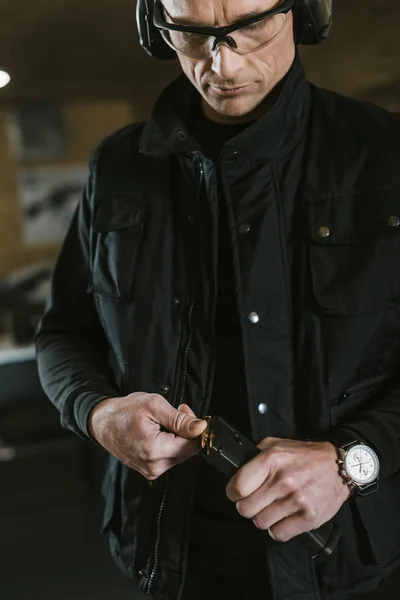 Handsome man putting bullet into rifle magazine — Stock Photo