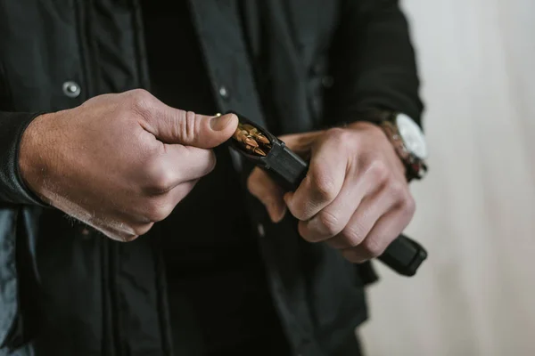 Cropped image of man putting bullet into rifle magazine — Stock Photo