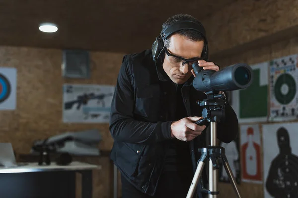 Mann blickt durch Fernglas auf ferngesteuertes Ziel im Schießstand — Stockfoto