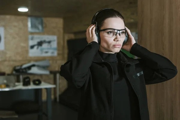 Attractive girl wearing hearing protectors in shooting range — Stock Photo