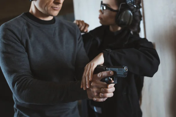 Cropped image of instructor describing client how to hold gun — Stock Photo