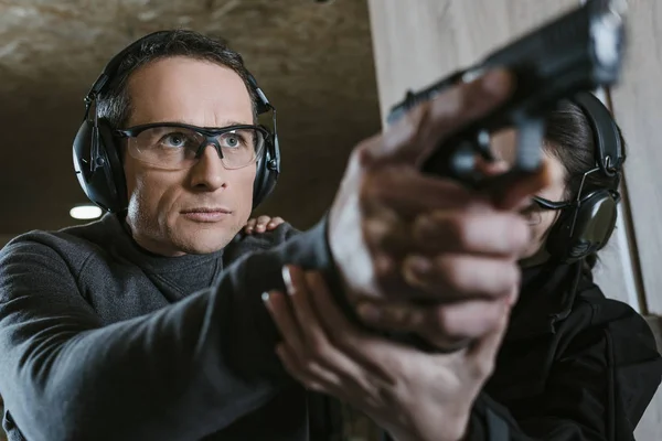 Instructor helping client to stand with gun in shooting range — Stock Photo