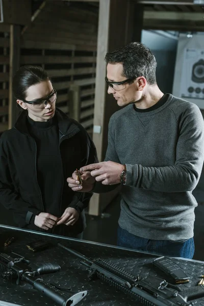 Instructor showing bullet to female client in shooting range — Stock Photo