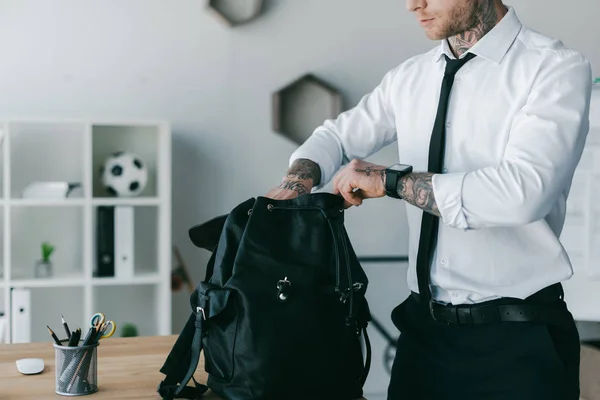 Cropped shot of young tattooed businessman opening backpack at workplace — Stock Photo