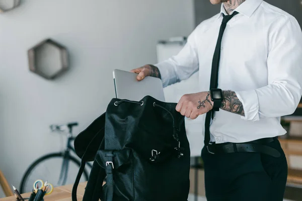 Обрізаний знімок молодого татуйованого бізнесмена, який кладе ноутбук у рюкзак — стокове фото