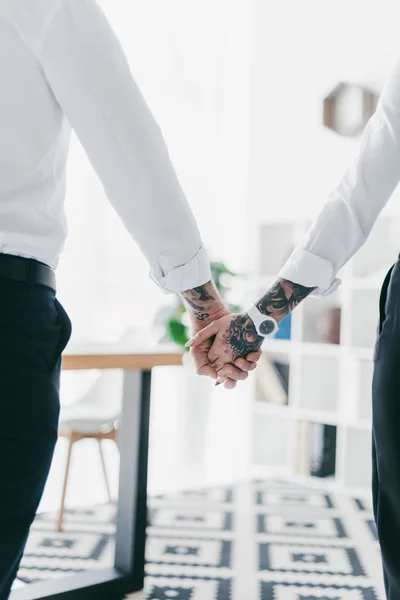 Partial back view of couple in formal wear holding hands in office — Stock Photo