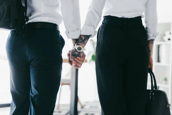 Cropped shot of couple in formal wear holding hands in office — Stock Photo