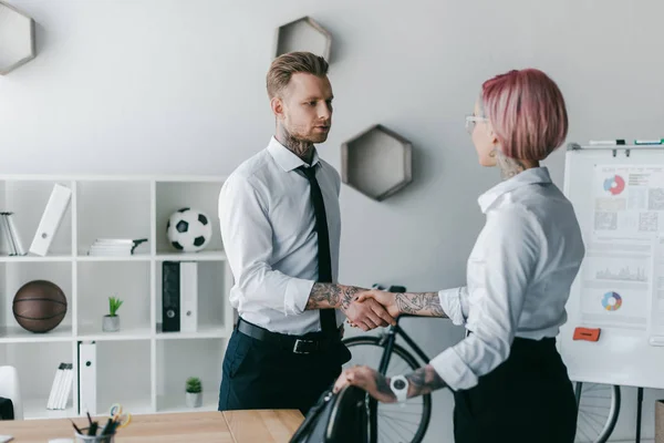 Young business people shaking hands and looking at each other in office — Stock Photo