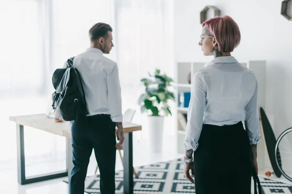 Вид сзади на молодую предпринимательницу, глядящую на красивого бизнесмена с рюкзаком, выходящего из офиса — стоковое фото