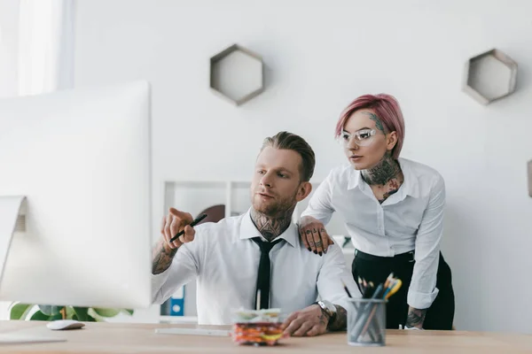 Jóvenes hombres de negocios tatuados mirando la computadora de escritorio en la oficina - foto de stock