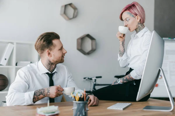 Молоді бізнес-колеги п'ють каву і дивляться один на одного в офісі — стокове фото