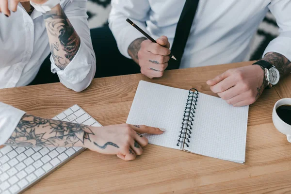 Cropped shot of young business people with tattoos taking notes together — Stock Photo