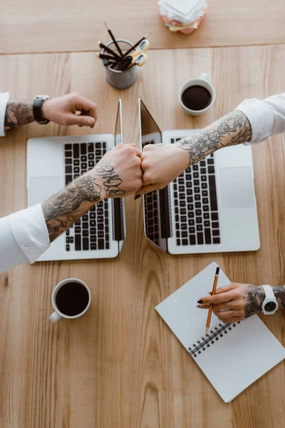 Top view of coworkers gesturing fist bump while working with laptops — Stock Photo