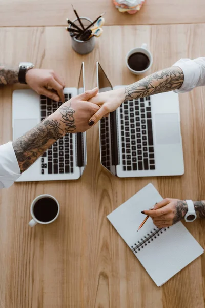 Cropped shot of colleagues shaking hands while using laptops — Stock Photo