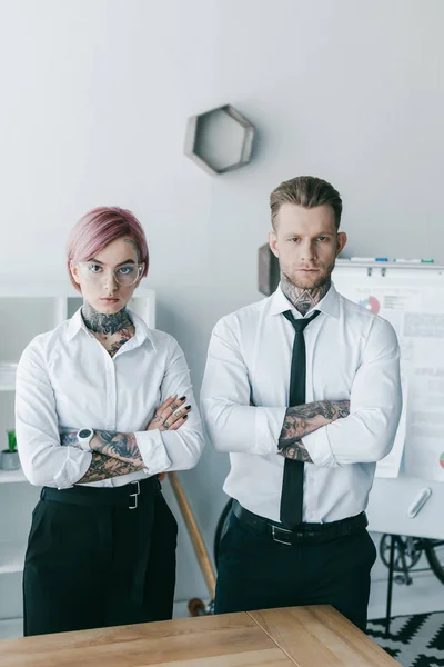 Jeunes hommes d'affaires confiants avec des tatouages debout avec les bras croisés et regardant la caméra — Photo de stock
