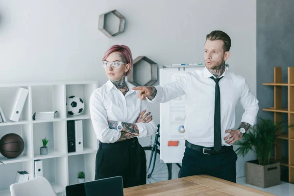Junge Geschäftsleute mit Tätowierungen, die wegschauen, während sie zusammen im Büro stehen — Stockfoto