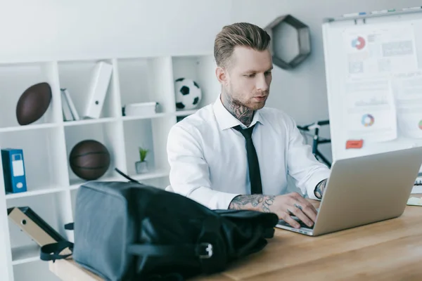 Schöner junger tätowierter Geschäftsmann mit Laptop im Büro — Stockfoto