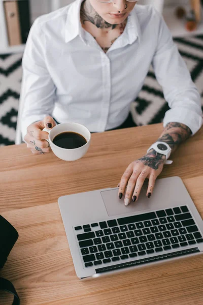 Colpo ritagliato di giovane donna d'affari in possesso di una tazza di caffè e utilizzando il computer portatile — Foto stock