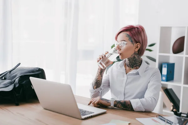 Молода бізнес-леді з татуюваннями питної води і використання ноутбука на робочому місці — стокове фото