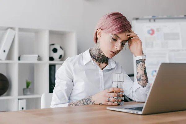 Müde junge Geschäftsfrau mit Wasserglas und Laptop im Büro — Stockfoto