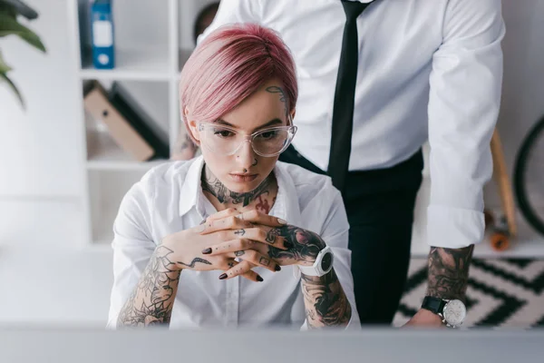 Focused young businesswoman sitting at workplace while male colleague standing behind — Stock Photo