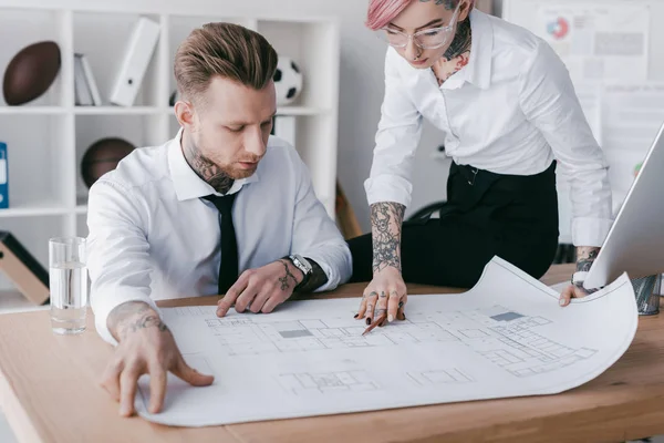 Focused young business people working with blueprint at workplace — Stock Photo