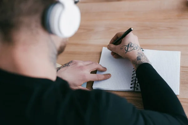 Selective focus of man in headphones taking notes at table — Stock Photo