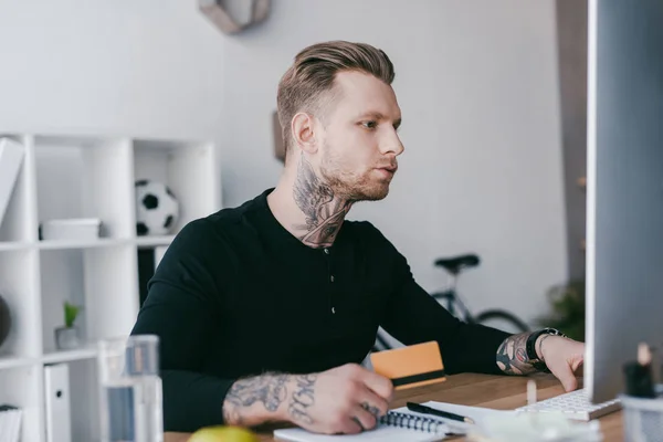 Jovem empresário segurando cartão de crédito e usando computador desktop — Fotografia de Stock