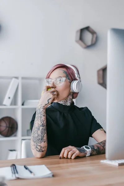 Junge Geschäftsfrau mit Kopfhörer und Brille schaut am Arbeitsplatz weg — Stockfoto