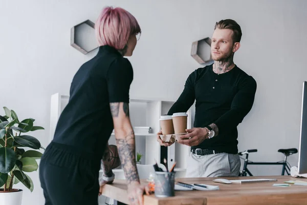 Beau jeune homme d'affaires donnant des tasses en papier à une collègue féminine au bureau — Photo de stock