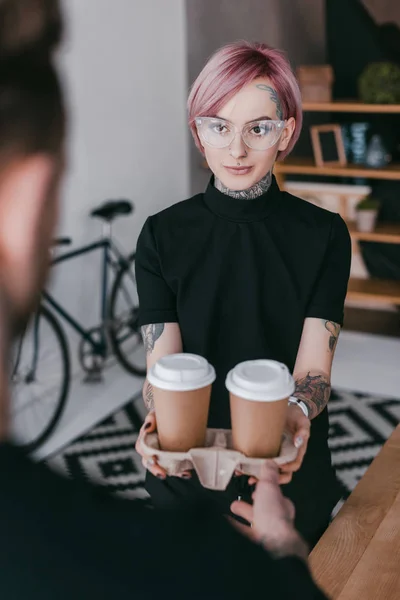 Plan recadré de jeune femme tatouée donnant des tasses en papier à un collègue — Photo de stock