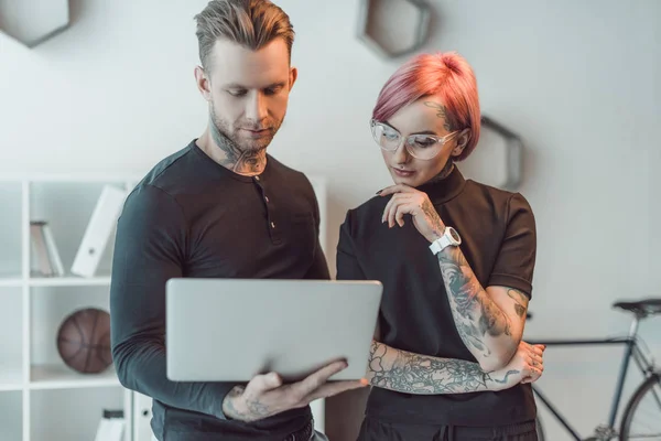 Молодые татуированные коллеги используют ноутбук вместе в офисе — стоковое фото