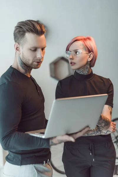 Jóvenes personas de negocios tatuados utilizando el ordenador portátil juntos en la oficina - foto de stock