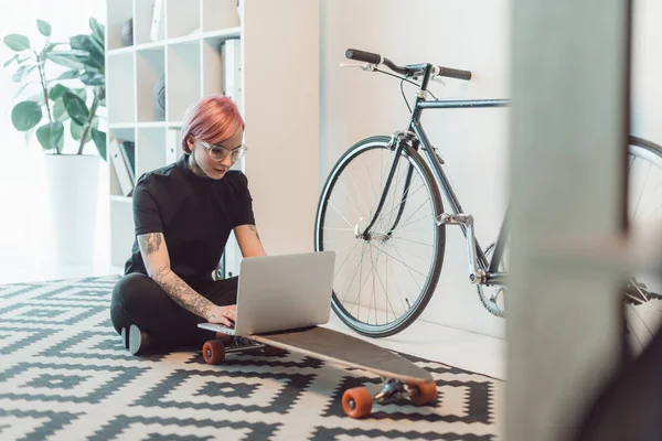 Young businesswoman in eyeglasses using laptop on skateboard — Stock Photo