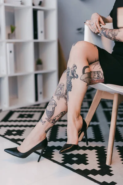 Cropped shot of young businesswoman with tattoos sitting on chair in office — Stock Photo