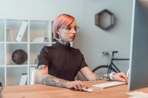 Giovane donna d'affari in occhiali utilizzando il computer desktop sul posto di lavoro — Foto stock