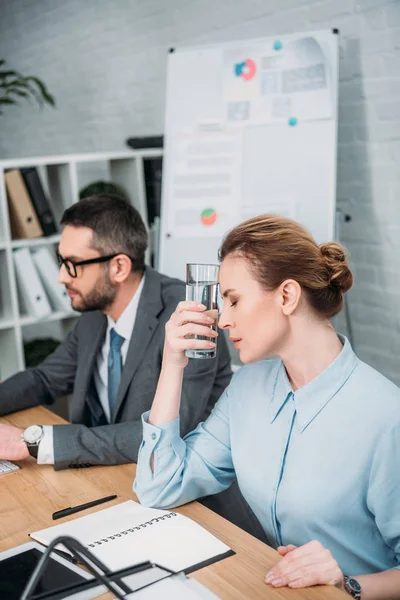 Erschöpfte Geschäftsfrau mit Kopfschmerzen beim Versuch, mit ihrem Kollegen im Büro zu arbeiten — Stockfoto