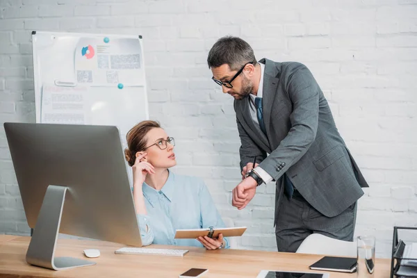 Jefe mostrando a su secretaria su reloj para explicar que ella llega tarde - foto de stock