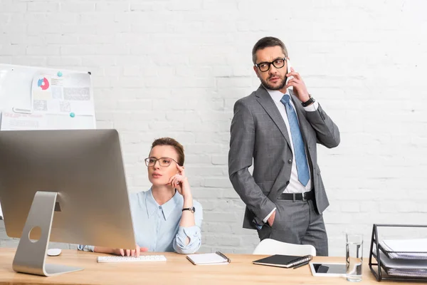 Бизнесмен разговаривает по телефону, пока его коллега пытается работать с компьютером — стоковое фото