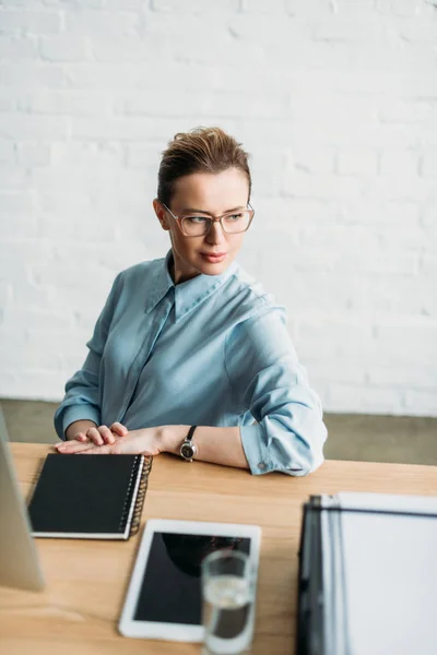 Stilvolle erwachsene Geschäftsfrau sitzt am Arbeitsplatz im Büro und schaut weg — Stockfoto