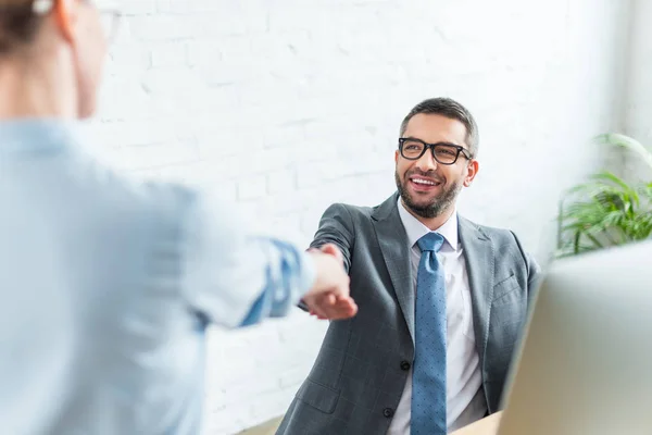 Hombre de negocios estrechando la mano de su colega mientras está sentado en el lugar de trabajo - foto de stock