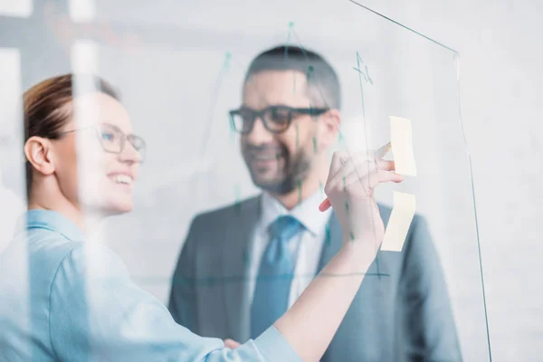 Lächelnde Geschäftspartner zeichnen Grafiken auf Glas-Präsentationstafel — Stockfoto