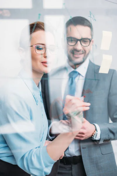 Happy businesspeople drawing graphs on glass presentation board — Stock Photo