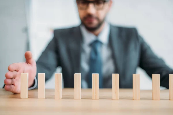 Primer plano plano del hombre de negocios ensamblando bloques de madera en fila en la mesa de trabajo, concepto de efecto dominó - foto de stock