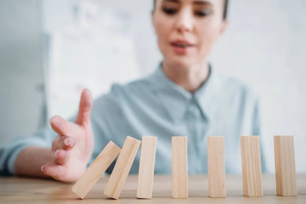 Close-up shot of businesswoman with falling wooden blocks in row on table, dominoes effect concept — Stock Photo