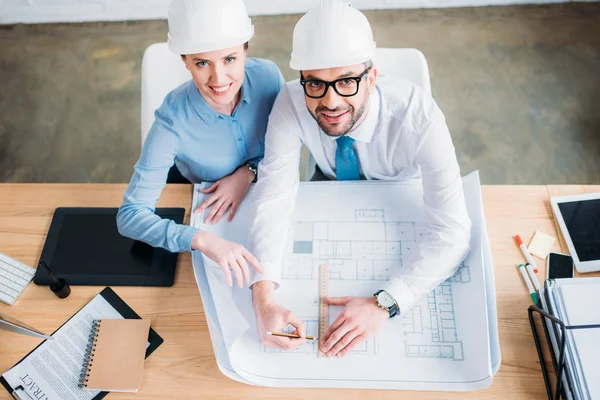 Vue grand angle des architectes travaillant avec le plan de construction au bureau et regardant vers le haut à la caméra — Photo de stock