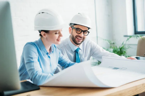 Arquitectos sonrientes trabajando con el plan de construcción en la oficina - foto de stock