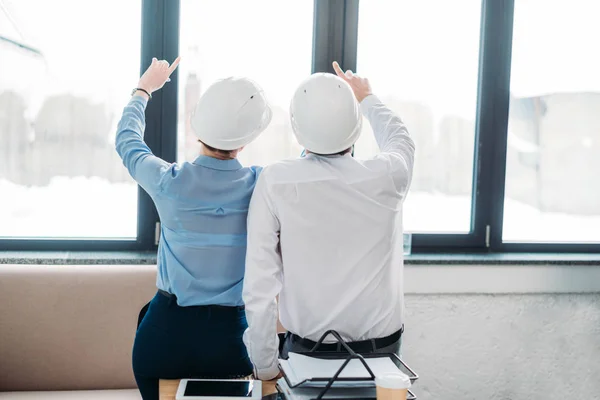 Vista trasera de los arquitectos apuntando hacia arriba a través de la ventana desde la oficina - foto de stock