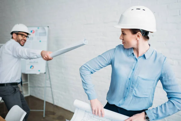 Arquitectos juguetones luchando con planos de edificios laminados en la oficina - foto de stock