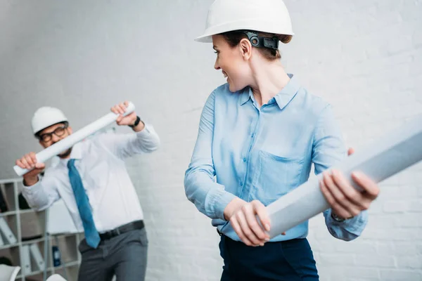 Zufriedene Architekten kämpfen im Büro mit gerollten Bauplänen — Stockfoto